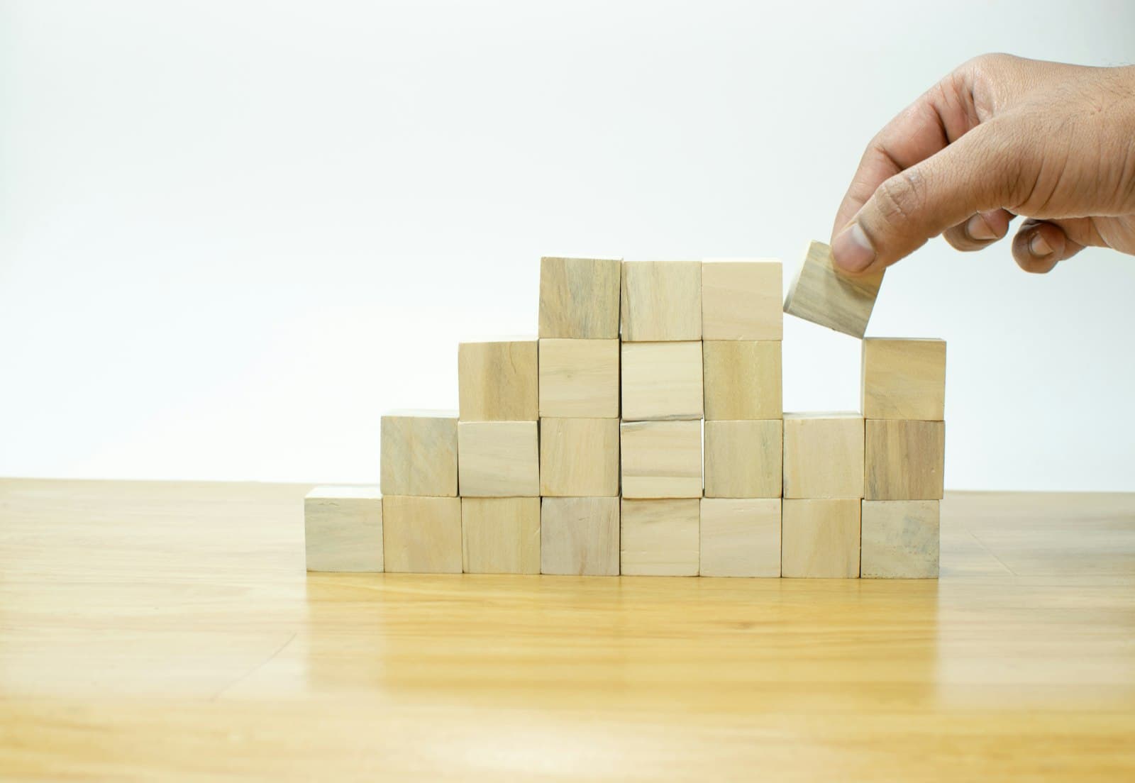 A hand placing the last wooden block on a neatly stacked wall of blocks