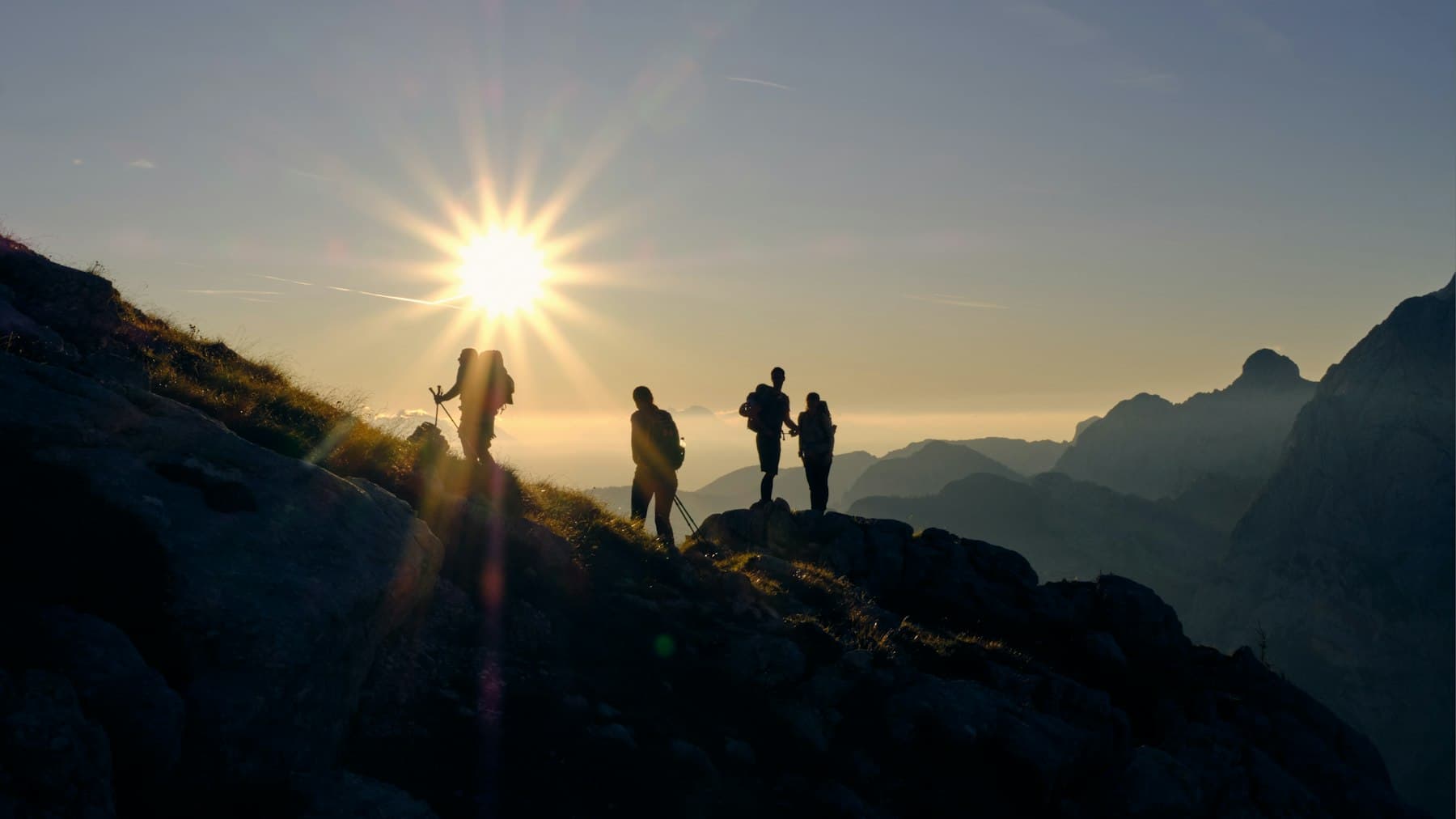 A small team climbing a mountain ridge toward the rising sun